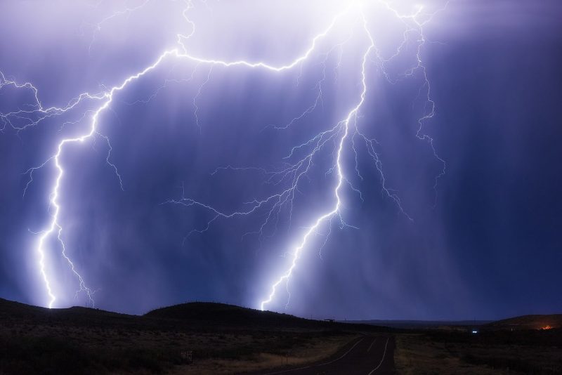 Lightning strikes over a road in the night sky.